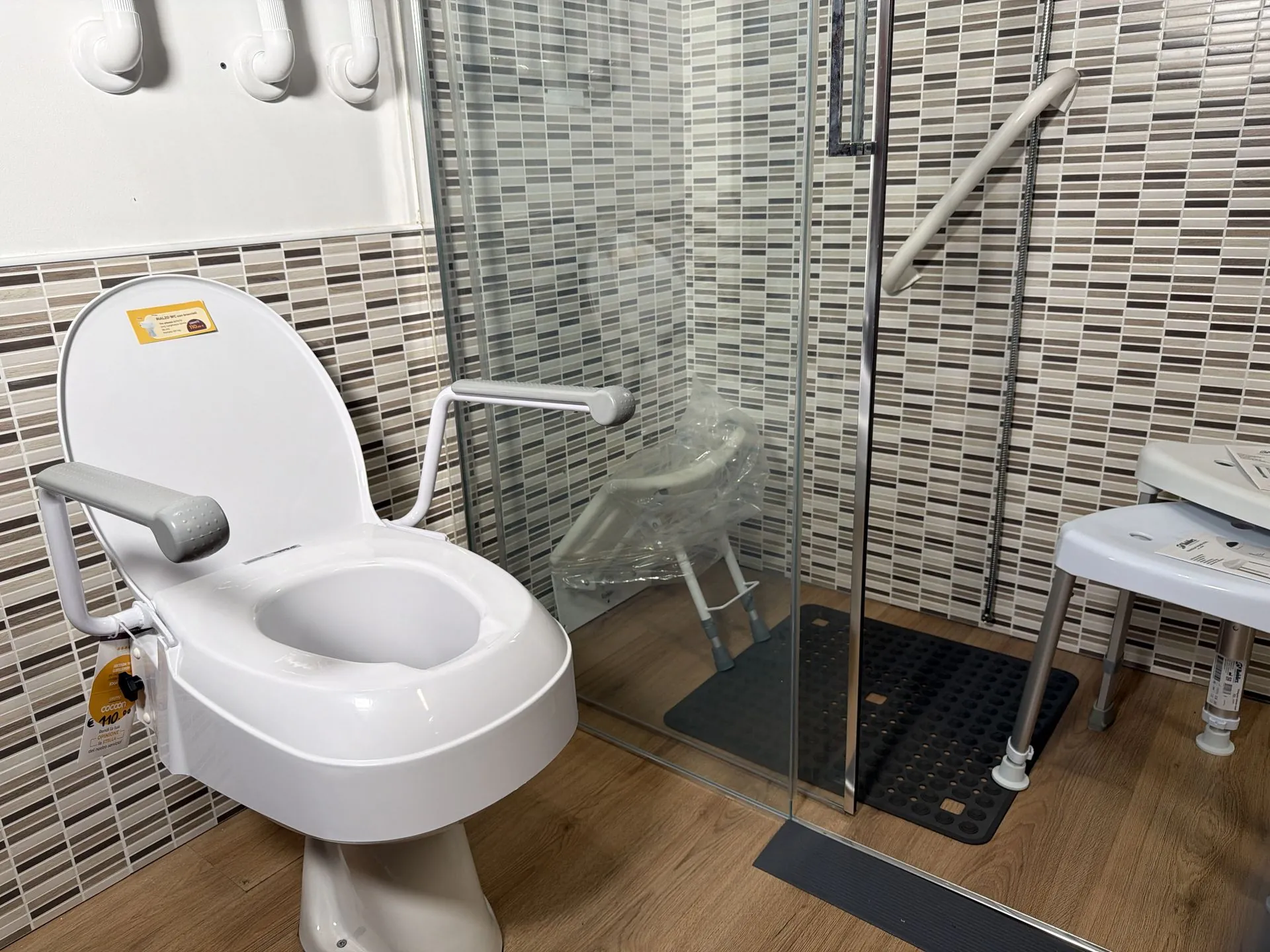 Accessible bathroom in the Cocoon showroom: raised toilet seat with armrests, level-access shower and stool