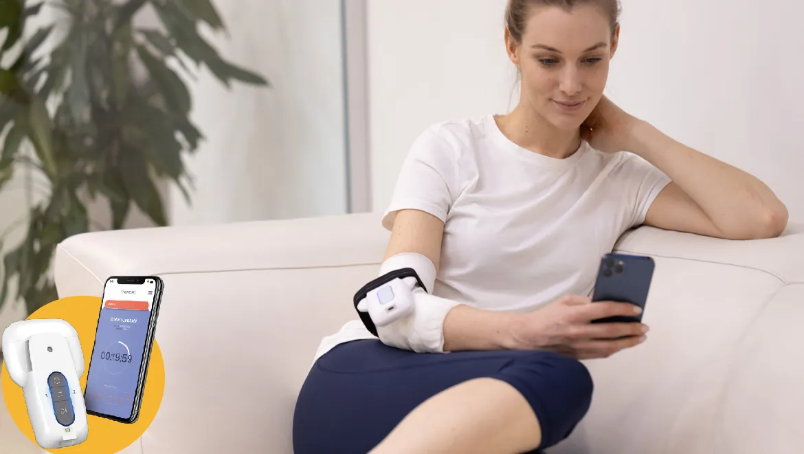 Donna sul divano con un apparecchio per magnetoterapia al gomito, controllato dallo smartphone