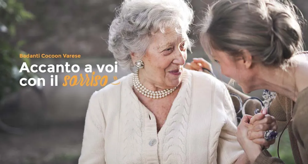 Signora anziana sorride a un’operatrice, con la scritta «Accanto a voi con il sorriso»