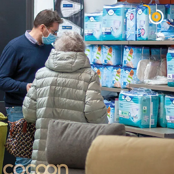 Signora anziana sceglie i pannoloni sugli scaffali del negozio Cocoon insieme a un operatore