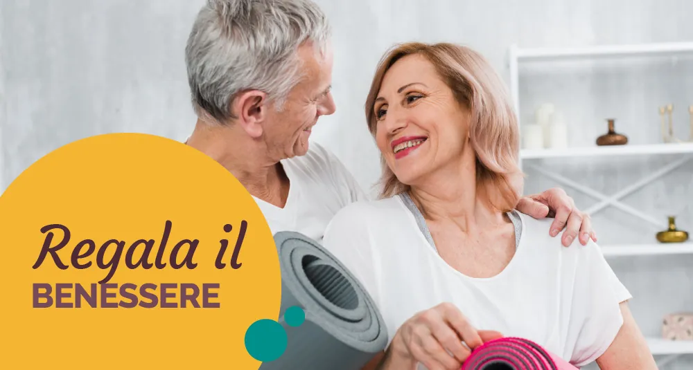 Coppia sorridente con i tappetini da ginnastica, con la scritta «Regala il benessere»