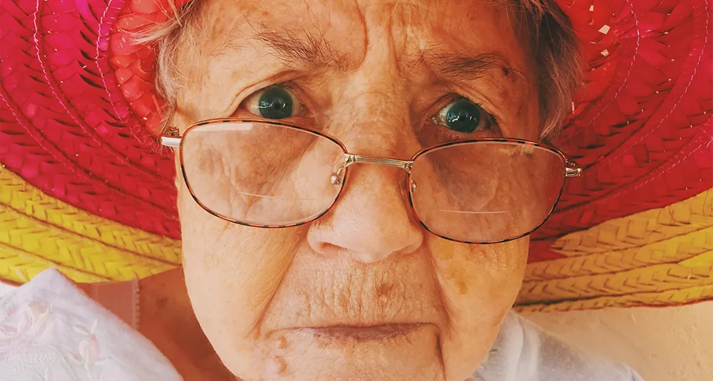 Primo piano di una signora anziana con gli occhiali e un cappello di paglia rosso
