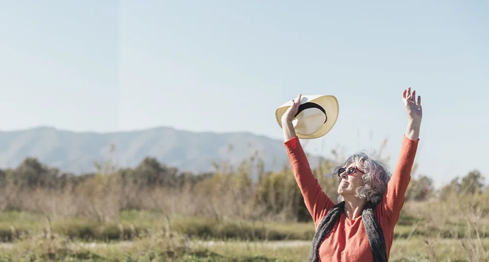 Signora anziana alza il cappello al cielo in un prato d’estate