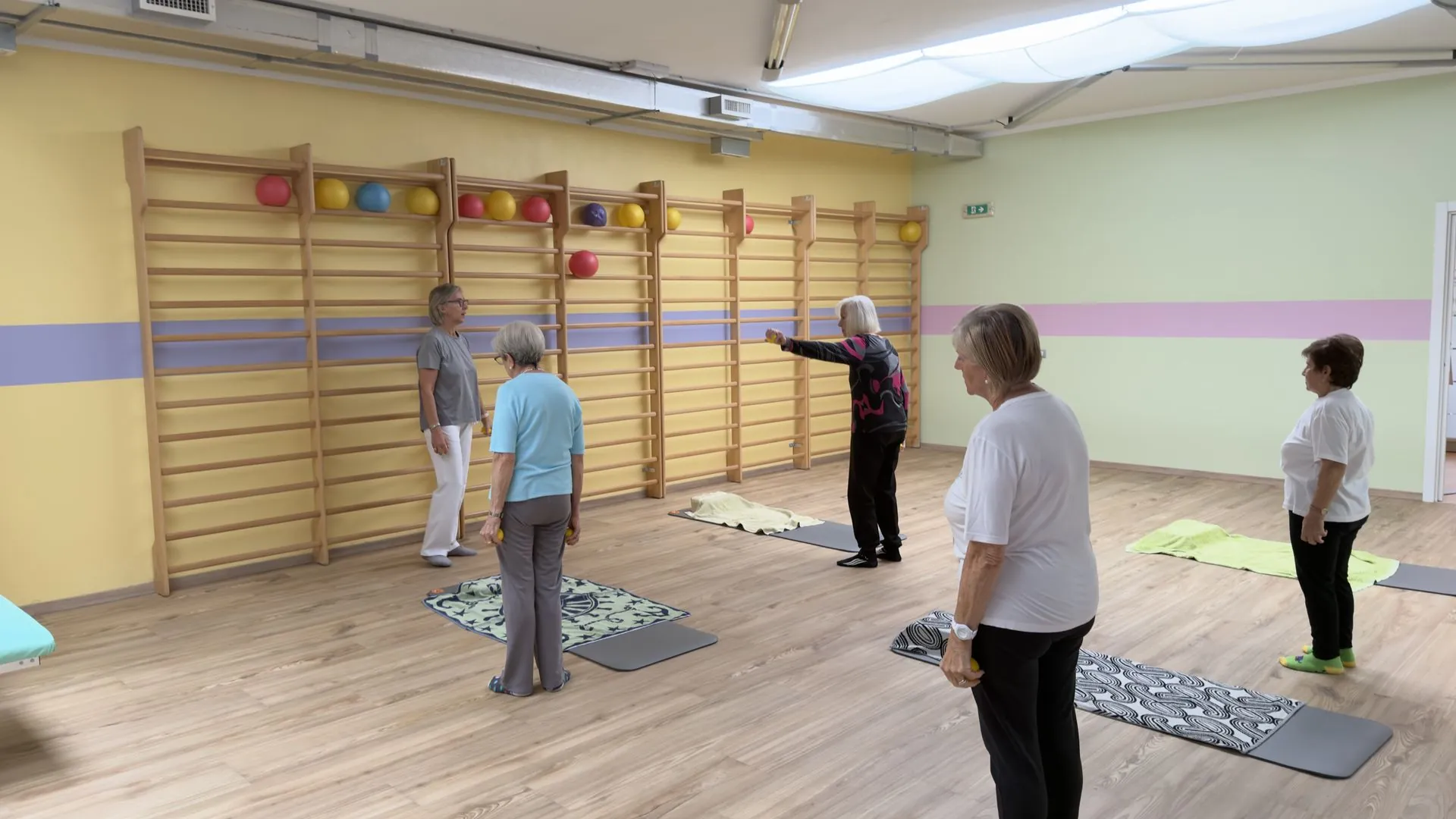 Esercizio di ginnastica dolce alla spalliera, con l’insegnante che segue il gruppo